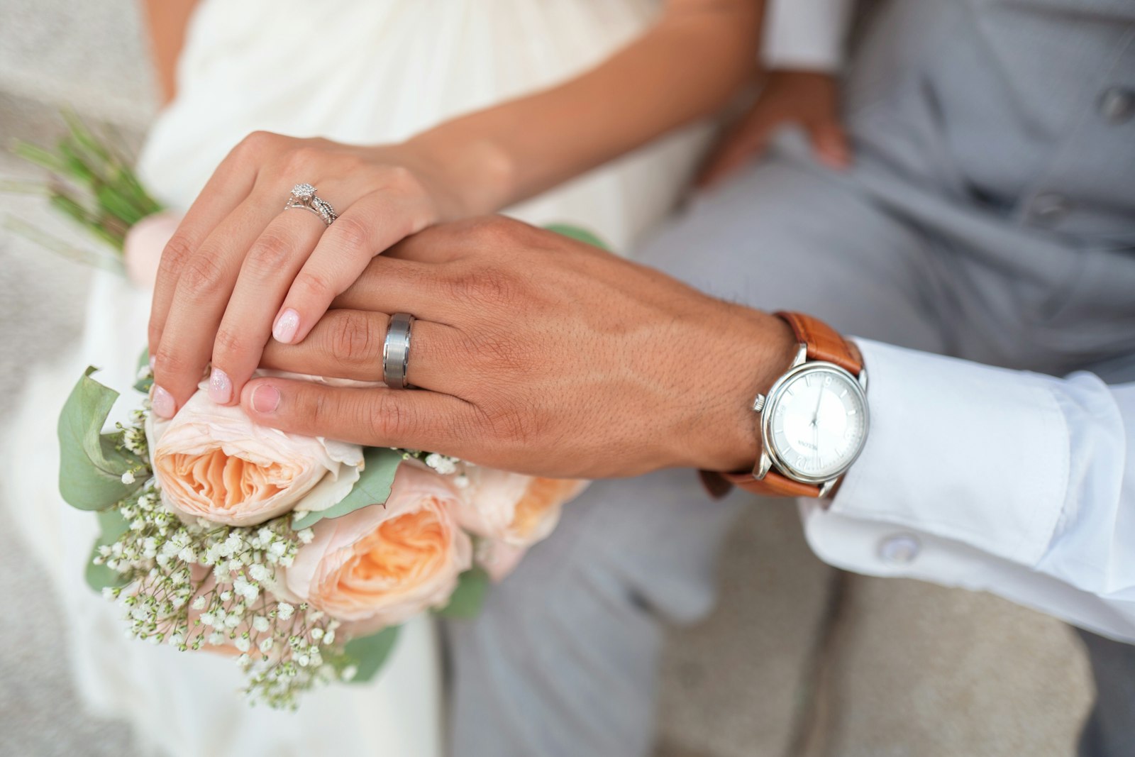 Bride and groom hands with peach garden rose bouquet and wedding rings